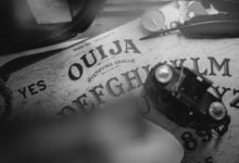 a ouija board with a quill, a candle, and a camera sitting on top of it